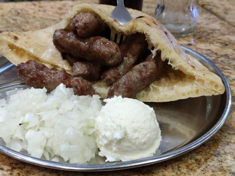 Sarajevski ćevapi u somunu s kajmakom i sjeckanim lukom na tradicionalnom tanjiru